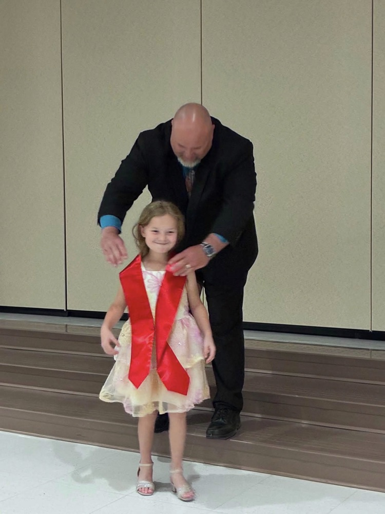 student in multi color dress with Dr. Conaway putting on a red sash