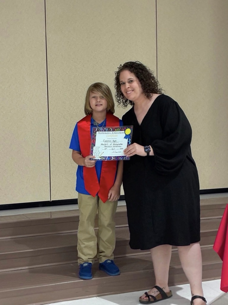 Student in tan pants blue shirt with Miss Wills putting on a red sash