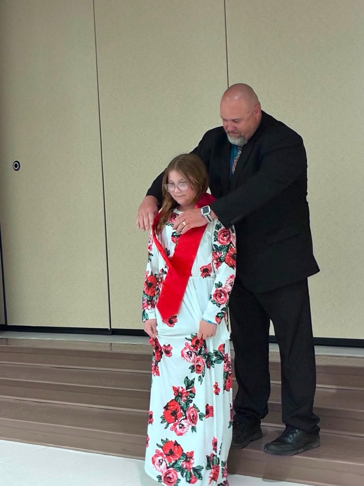 student in white and red flower dress with Dr. Conaway putting on a red sash