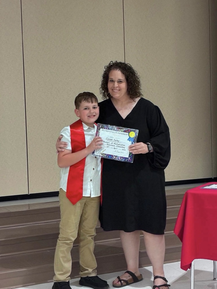 student in tan pants white shirt with Miss Wills putting on a red sash