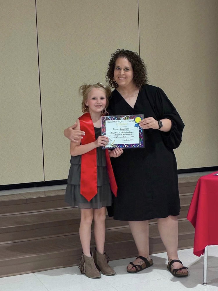student in gray dress with Miss Wills putting on a red sash