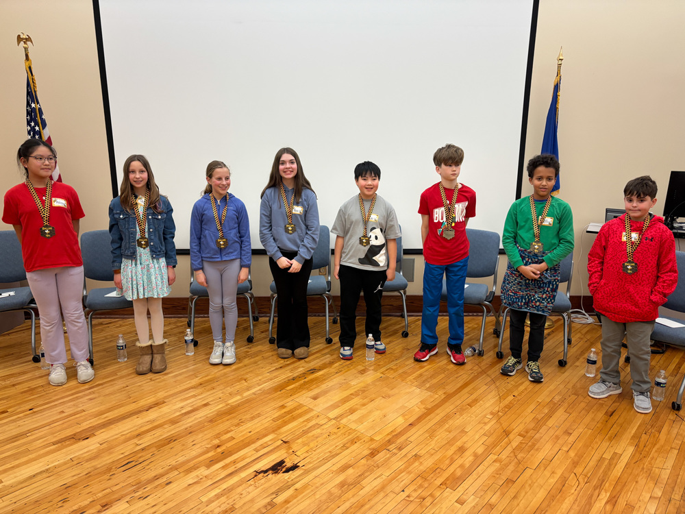 9 participants of the MCPS spelling bee standing for a picture. Each student is wearing a medal.
