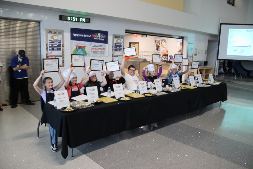 Students sitting at a table holding up certificates