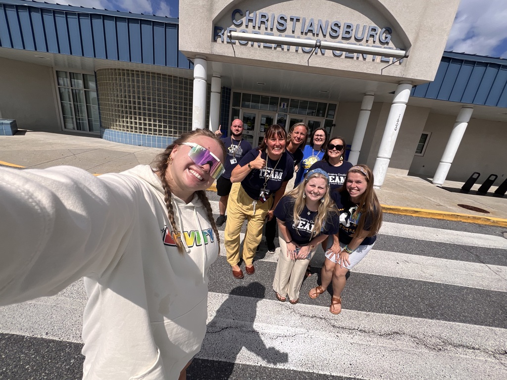 A group of smiling CES staff members pose for a selfie outside the Christiansburg Recreation Center on a sunny day.