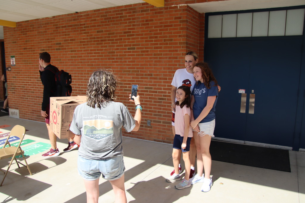 A student-athlete poses with two smiling visitors while another person takes their photo.