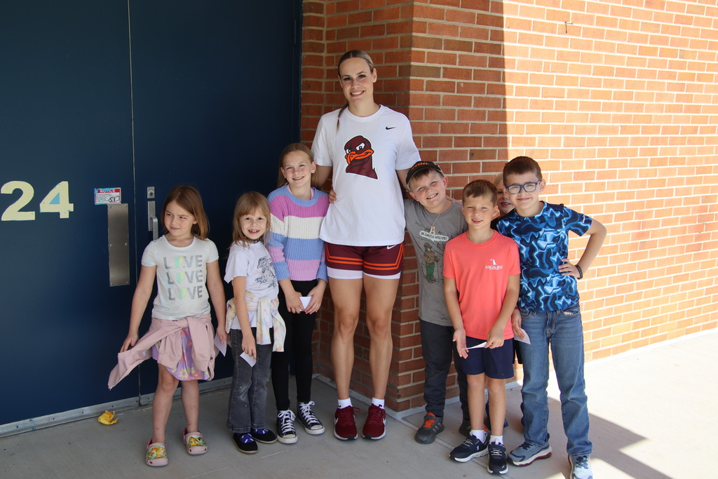A Virginia Tech student-athlete poses with a group of smiling elementary school children.