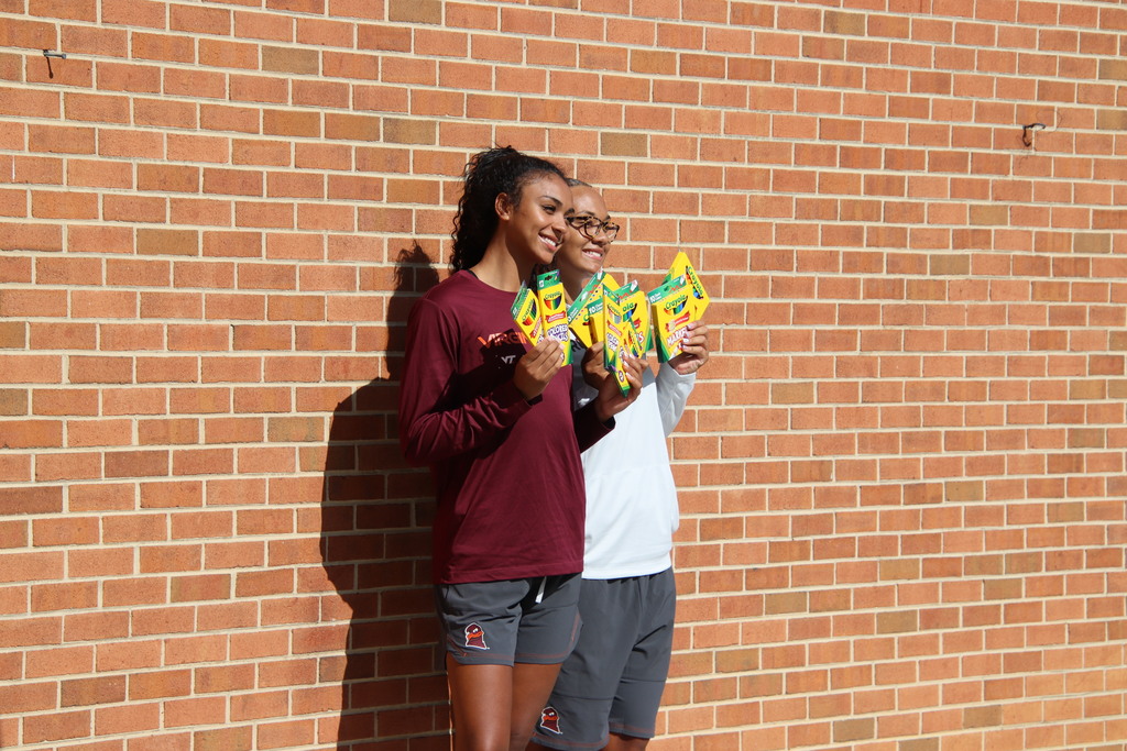 Two Virginia Tech student-athletes smile while holding boxes of colorful school supplies.
