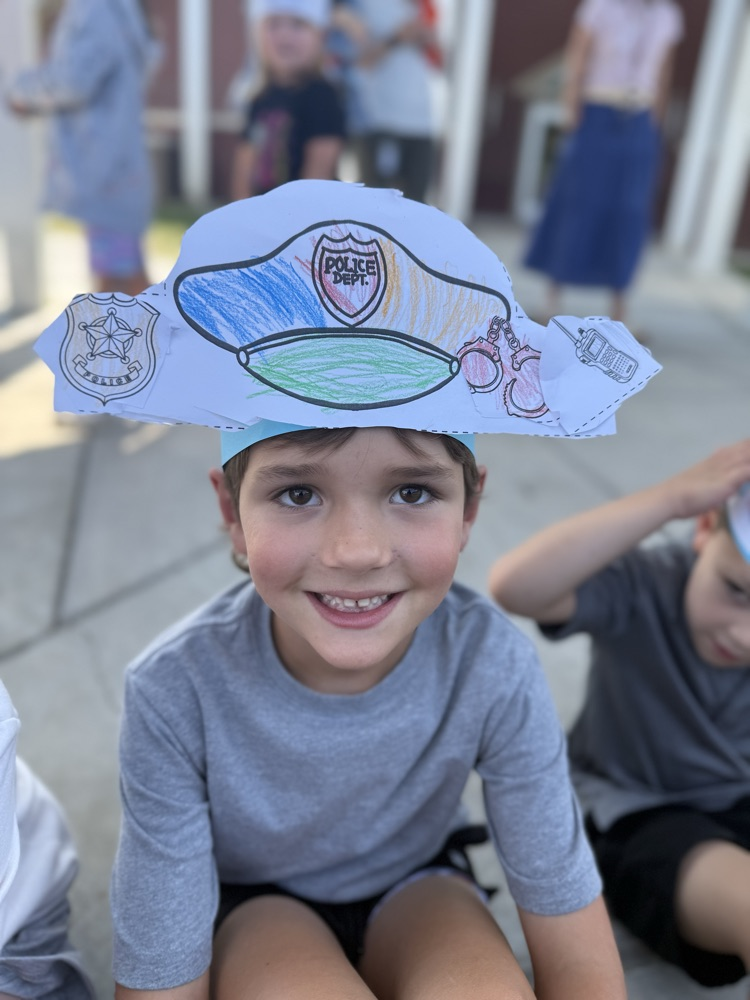A smiling young boy wearing a paper police hat outdoors.
