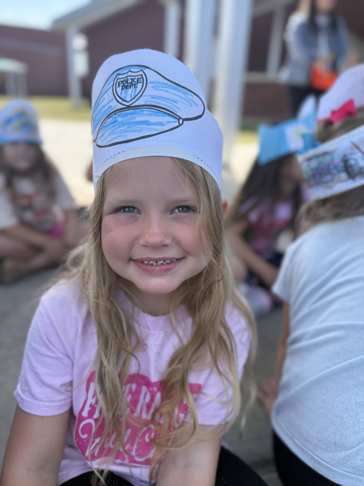 A smiling young girl wearing a paper police hat outdoors.