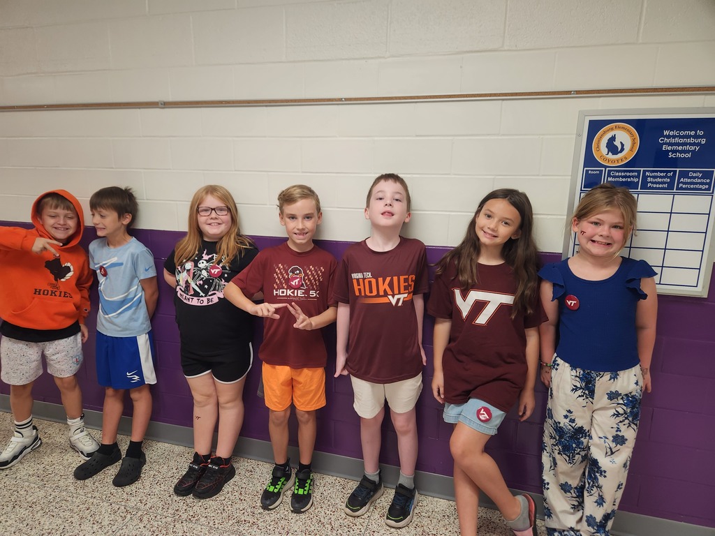 Smiling elementary students lined up to display their shirts from their favorite college