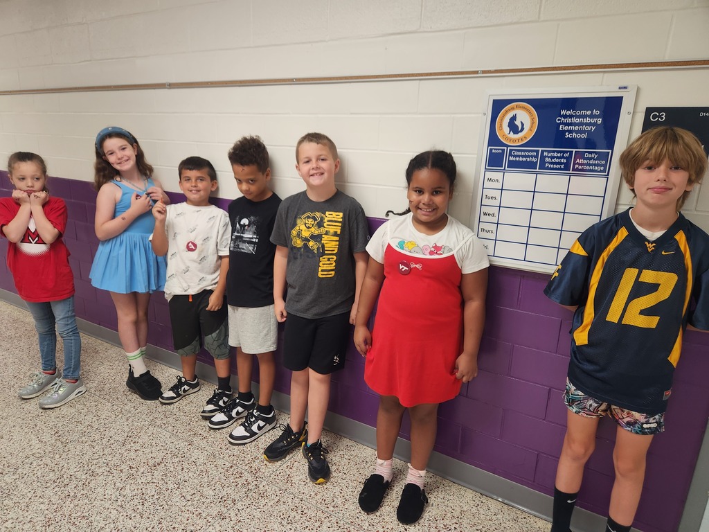 Smiling elementary students lined up to display their shirts from their favorite college