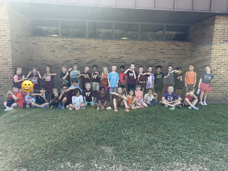 A large group of second grade students pose outside wearing various college tshirts