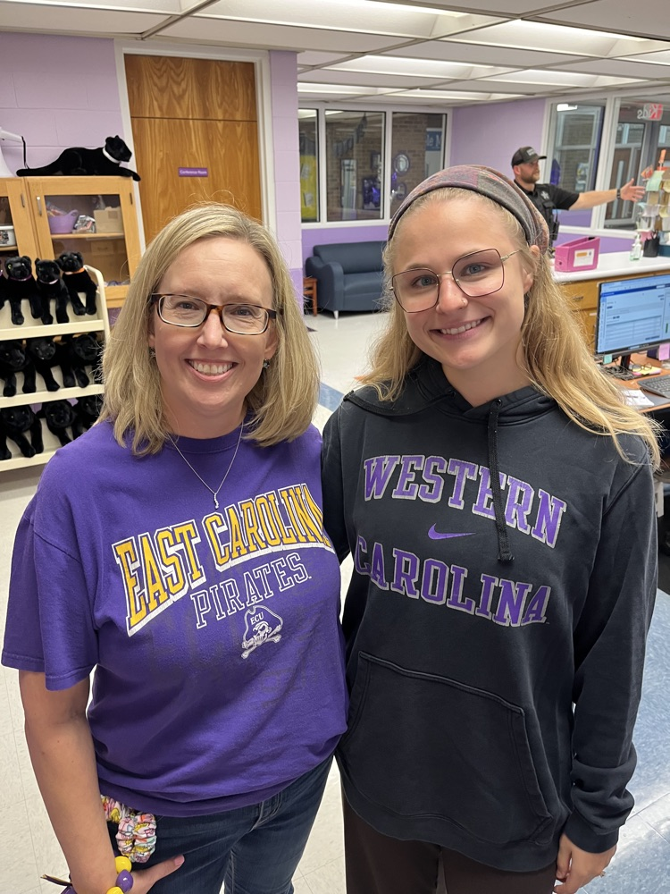two teachers smile in the office wearing and east Carolina and western Carolina shirt