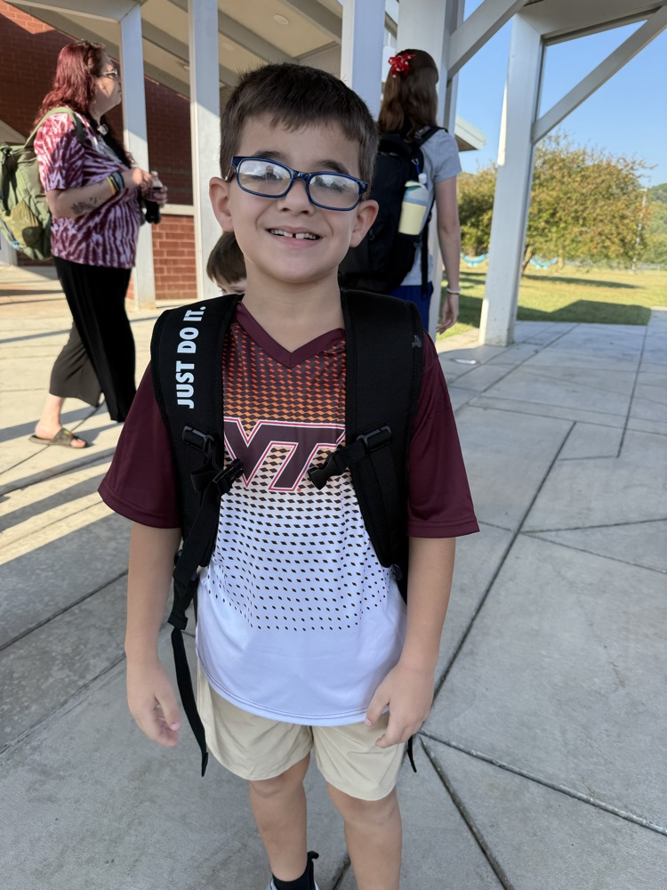Young boy with glasses wearing a black backpack and a maroon and white Virginia Tech jersey outside.