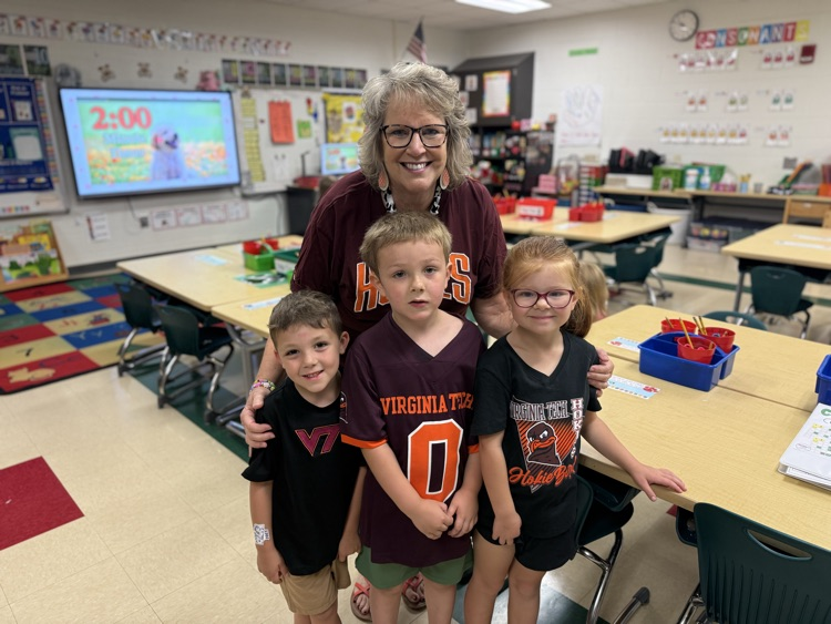 Teacher posing in a classroom with three young students wearing Virginia Tech shirts.