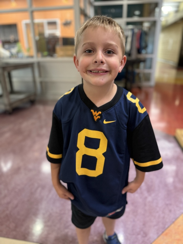 Young boy smiling in a blue West Virginia #8 jersey indoors.