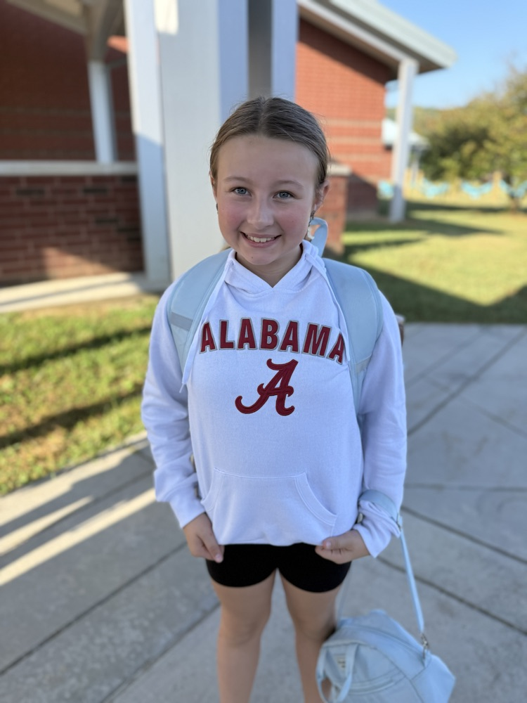 Older girl smiling outside in a white Alabama "A" hoodie and light blue backpack.