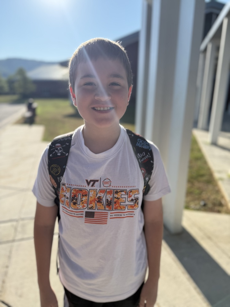 Smiling boy with a backpack outdoors wearing a white Virginia Tech Hokies t-shirt.