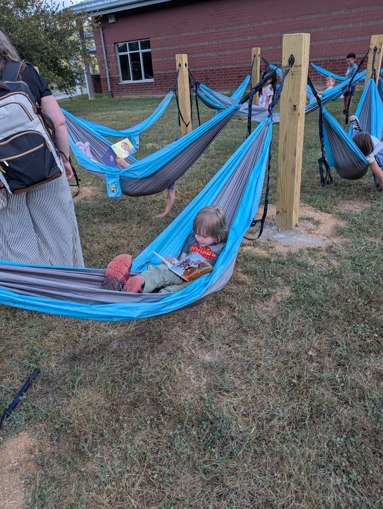 A young boy lying in a hammock while reading a book outdoors.