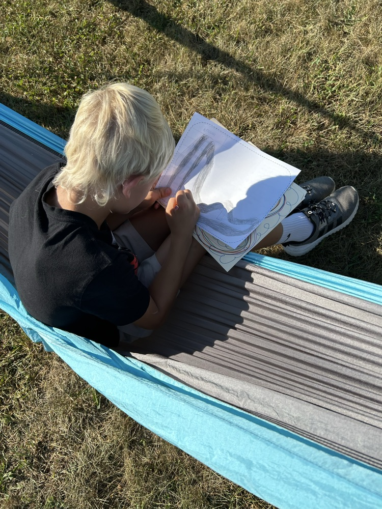 Overhead view of a boy writing on a worksheet while reclining in a blue hammock.