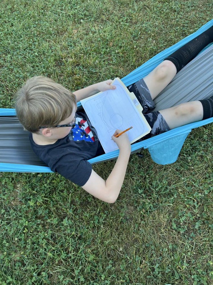 Overhead view of a boy writing on a worksheet while reclining in a blue hammock.