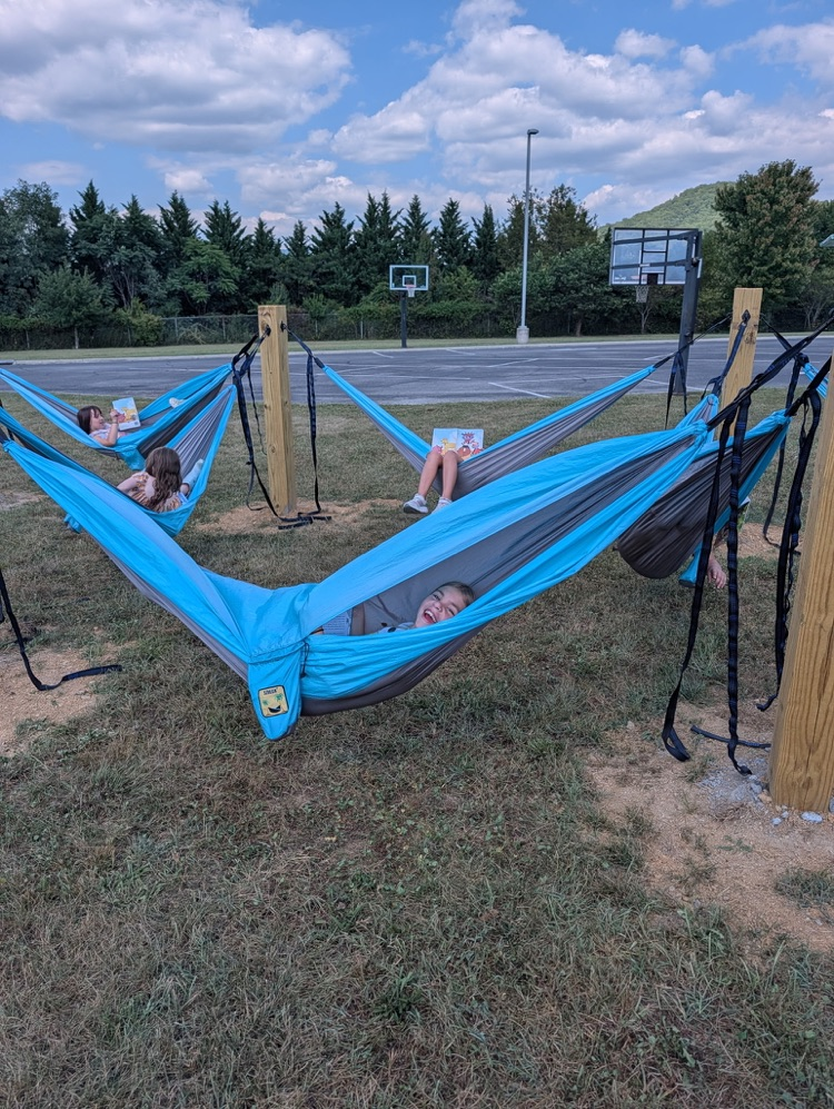 A child smiling while lying in a hammock outdoors near a playground area.