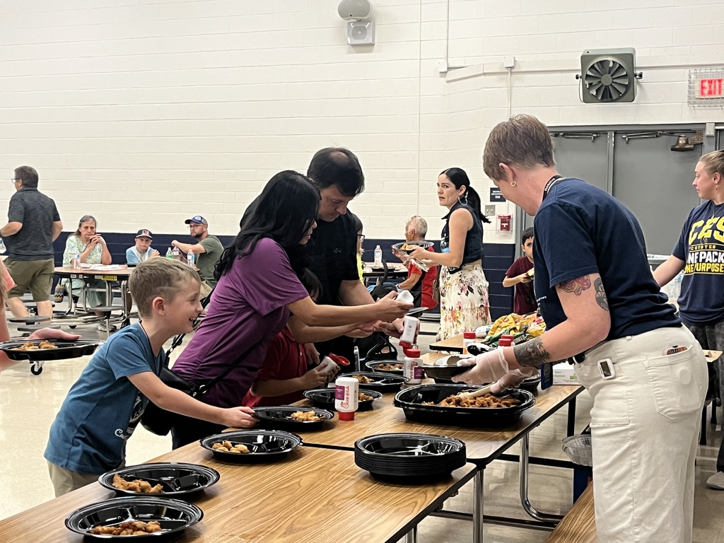 Students and families move through a dinner serving line during Literacy Night as CES staff members serve food in the cafeteria.