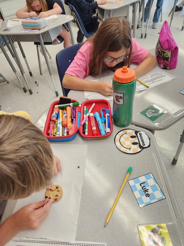 3 elementary students sitting at desks simulating recovering fossils with chocolate chip cookies while following the scientific process