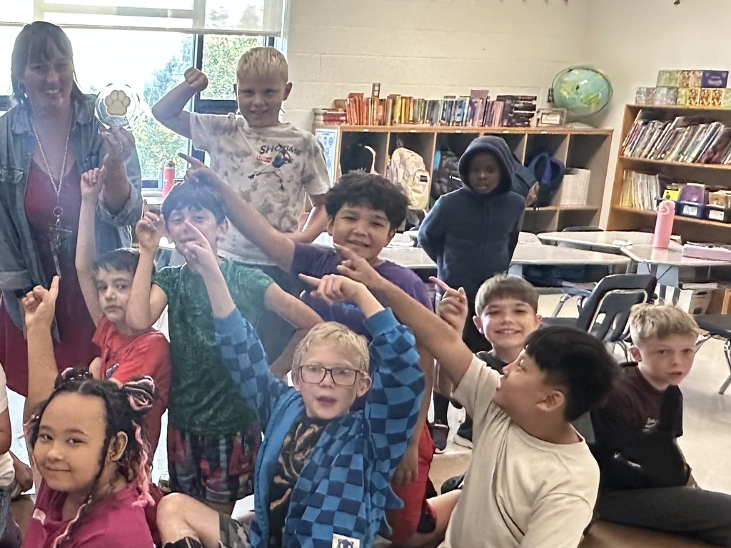 A group of happy elementary students pointing toward their teacher and smiling!