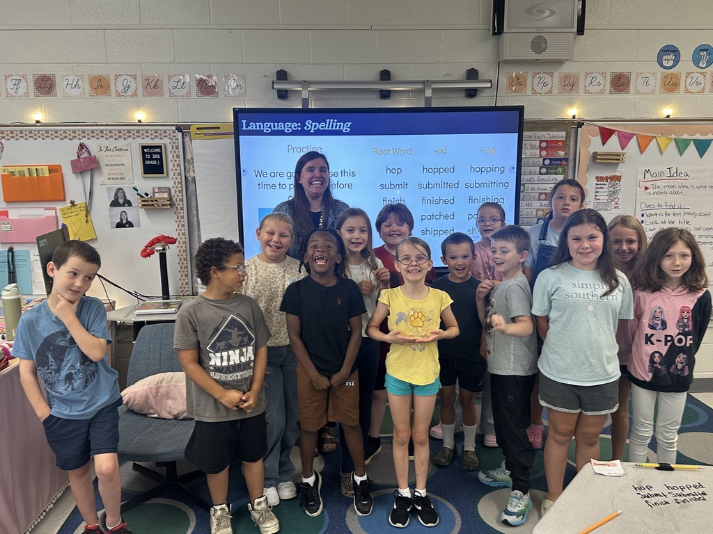 A group of smiling elementary students standing around their teacher, happy because they won a contest.