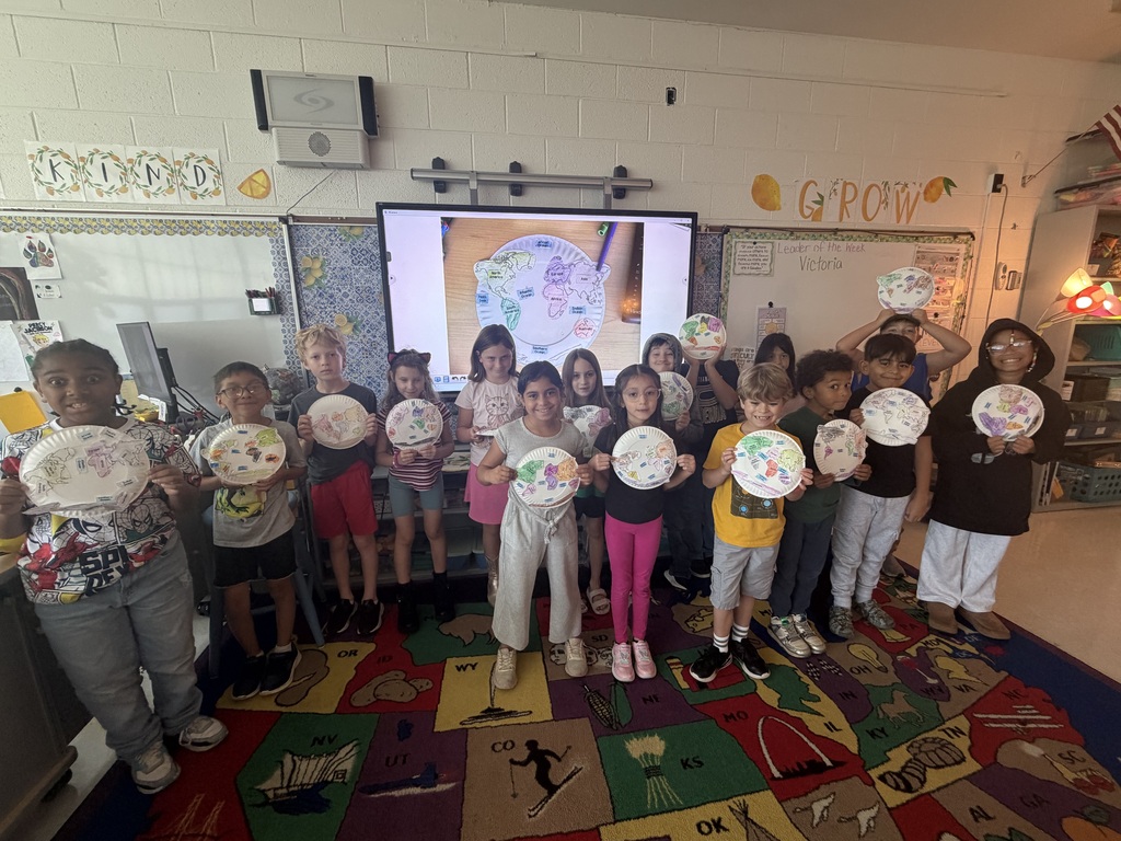 A group of elementary students standing in front of a viewboard showing the maps they created of continents and oceans using paper plates.