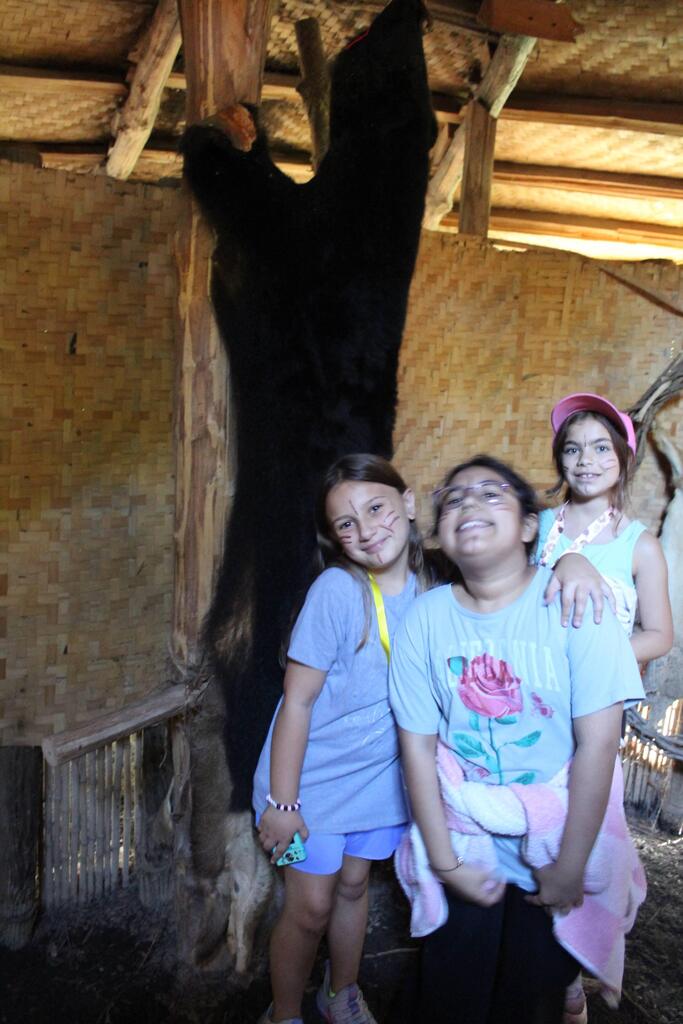 Three smiling studnets posing in front of a bear hide in a native american museum.