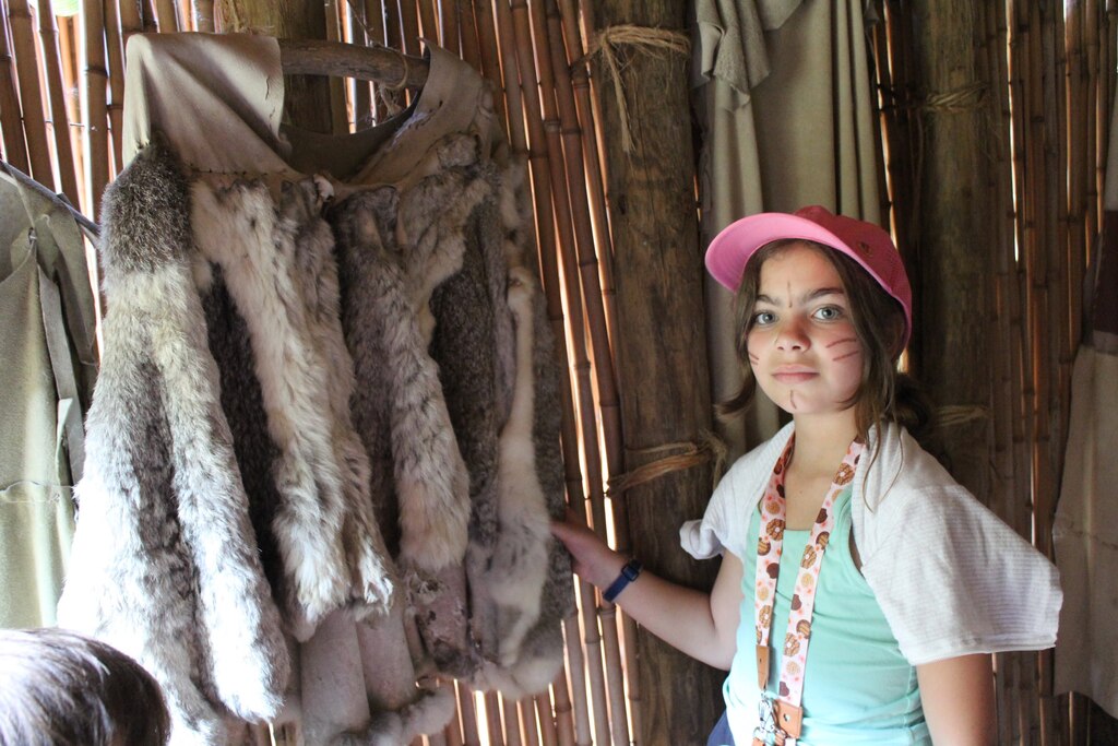 Student standing in front of animal pelts in a hut in a native american indian village.