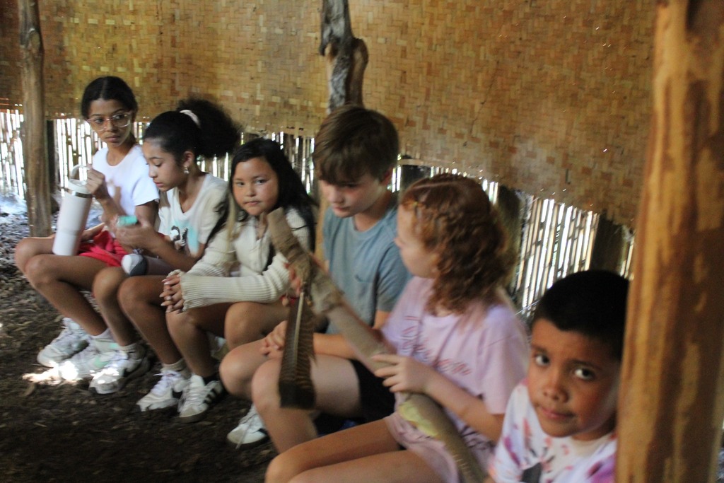 Elementary students sitting in a hut in a native american village museum.