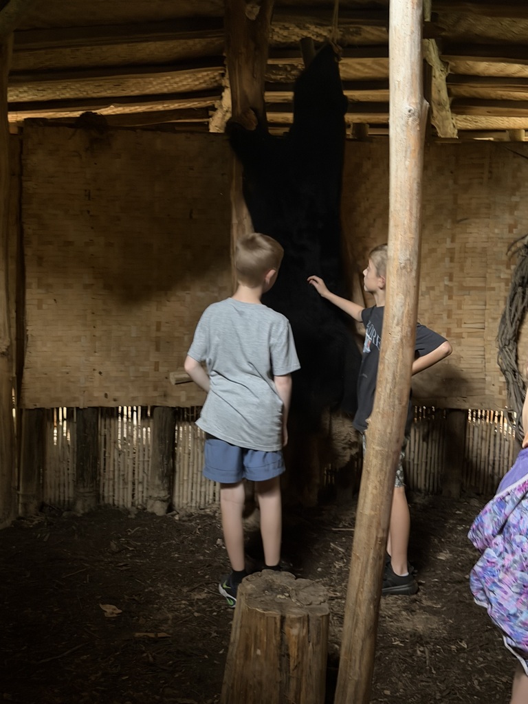 Smiling student learning about native americans in a native american building where a bear skin is hanging.
