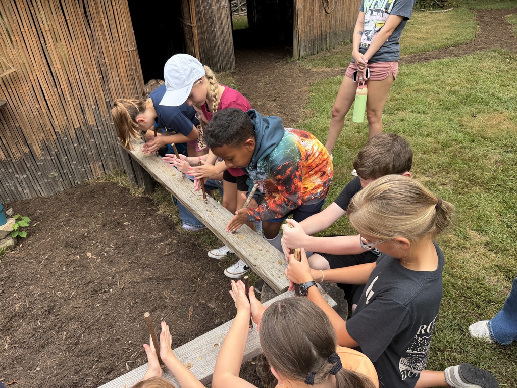 Elementary students learning about typical daily native american work near a garden.