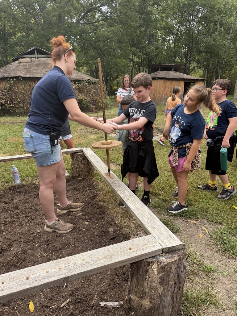 Elementary students learning about typical daily native american work near a garden.