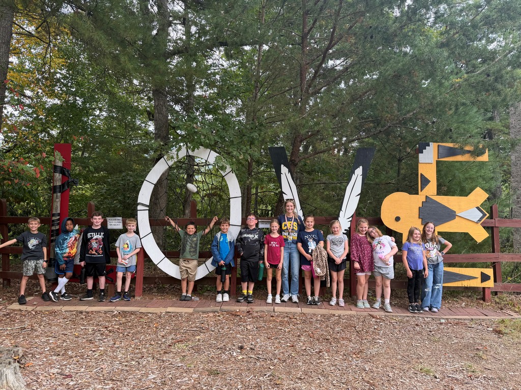 Smiling group of elementary school students at an outdoor indian village museum, in front of a mural spelling love.