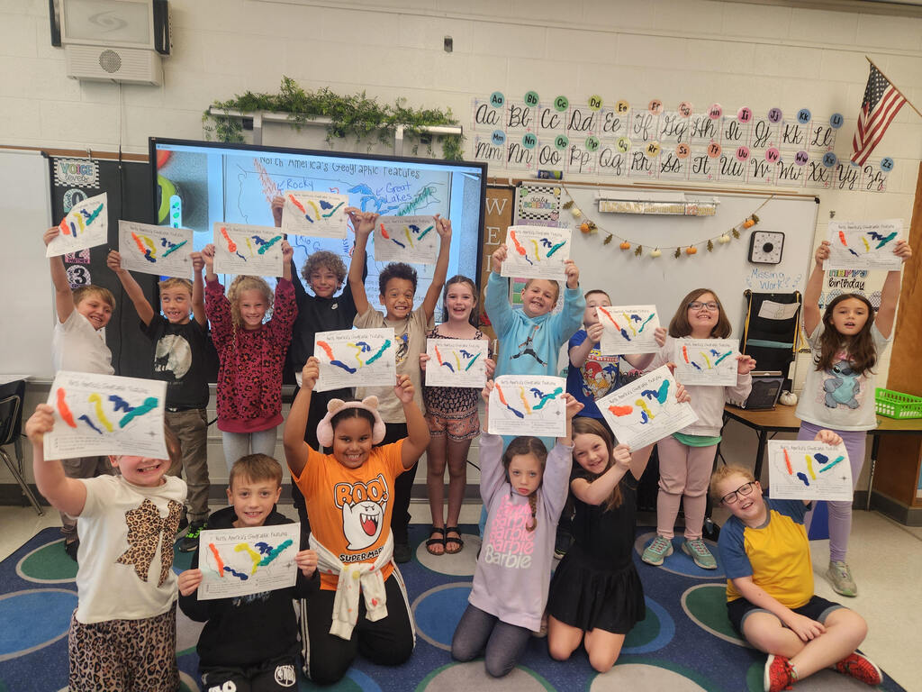 Smiling elementary students showing off their colorfull 3D maps of North America.