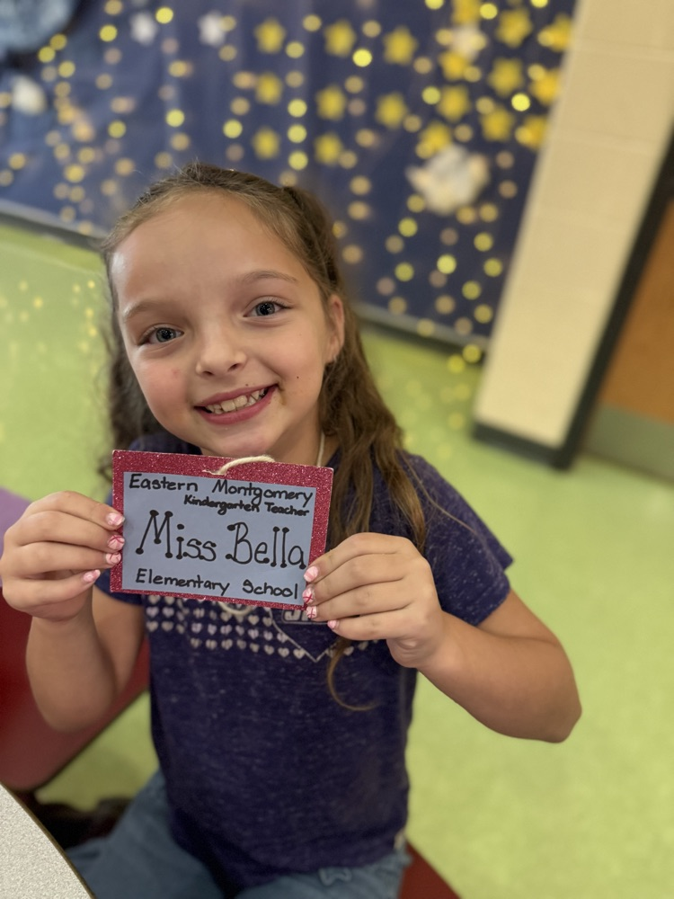 A young girl smiling as she holds up a glittery name tag that reads "Miss Bella".