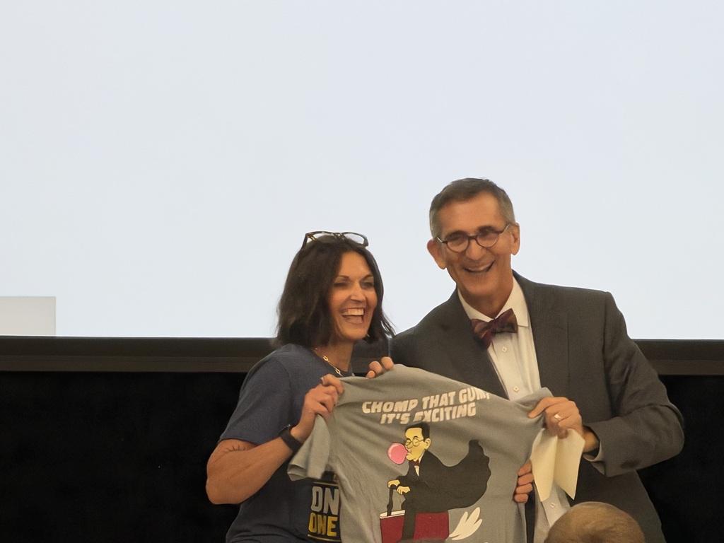 Smiling elementary principal with a smiling professional in a gray suit in an elementary school setting.