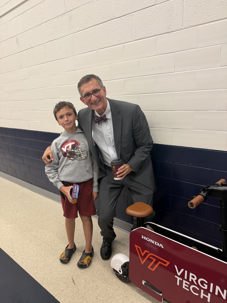 Smiling elementary student with a smiling professional in a gray suit in an elementary school setting.