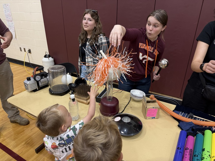 Demonstrators and children interacting with a Van de Graaff generator static electricity experiment.