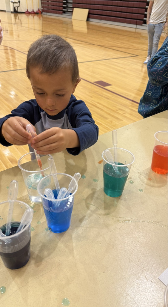 A young boy using a liquid pipette to mix colorful liquids in plastic cups.