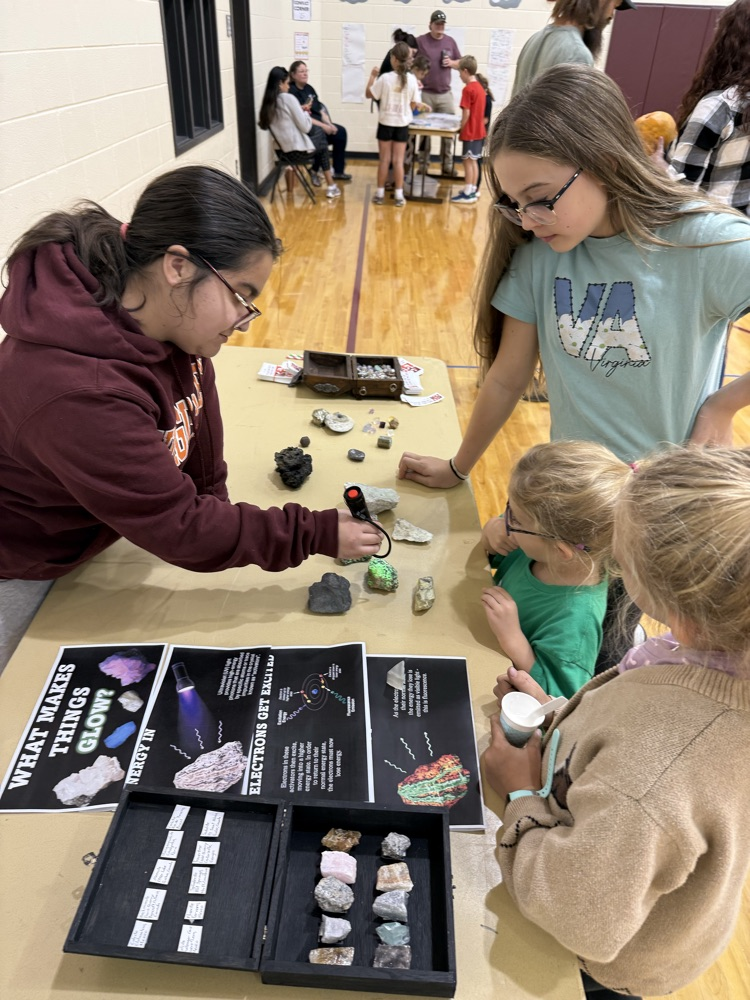 A demonstrator using a UV light to show glowing minerals to young students at a science display.
