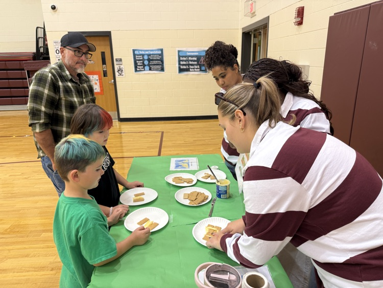 Students and adults gathered at a table examining graham cracker and peanut butter models.