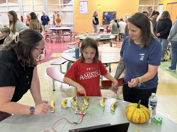A young student touching bananas wired together in a circuit demonstration with two adults.
