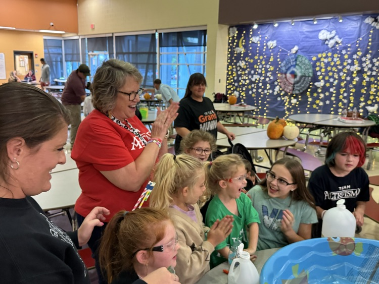A teacher and group of students enthusiastically gathered around a hands-on activity table.