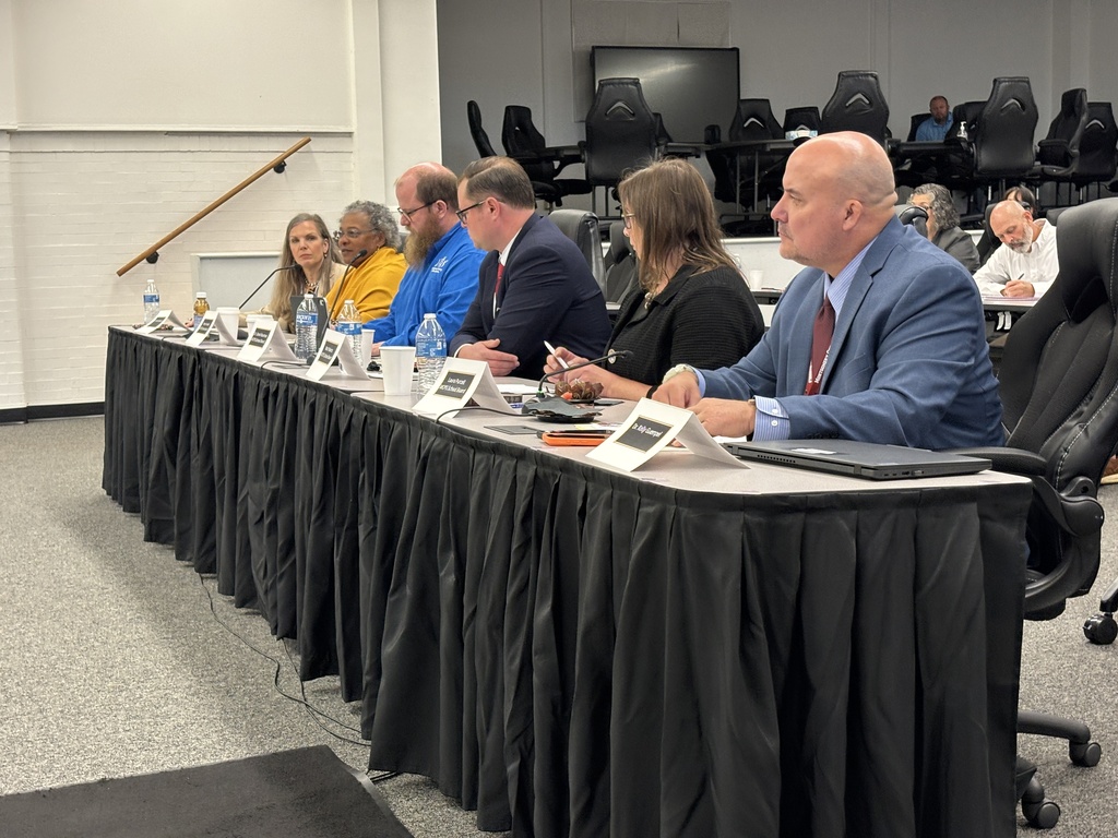 Members of the Montgomery County Public Schools Board seated along a long, black-draped table listening intently and taking notes during a legislative meeting
