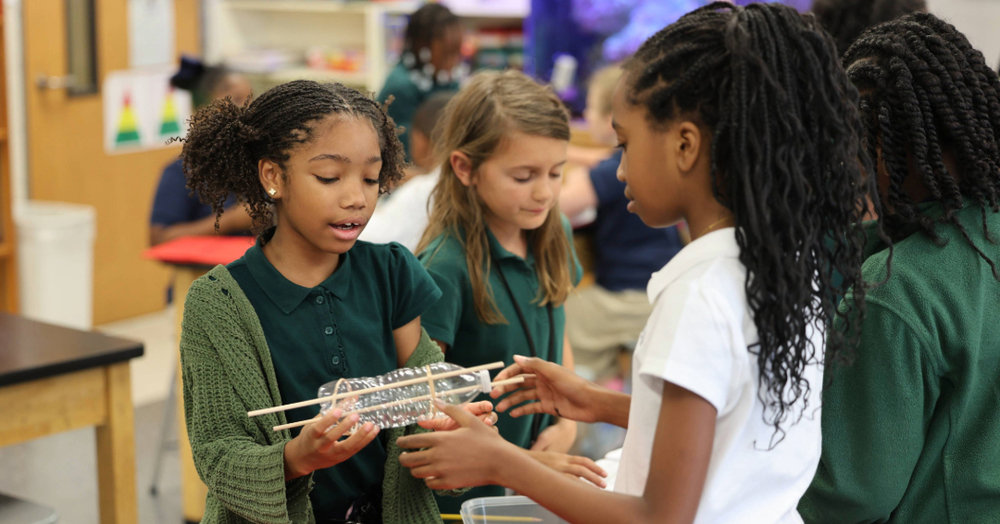 Four elementary students leaning in together over schoolwork. Above them, large blue text reads "U.S. News & World Report TOP 25." At the bottom, a "Best Elementary Schools U.S. News Rankings" badge is shown alongside school logos with ranking stars: Forest Avenue Academic Magnet ranked #1, Bear Exploration Center ranked #10, and MacMillan International Academy ranked #12.